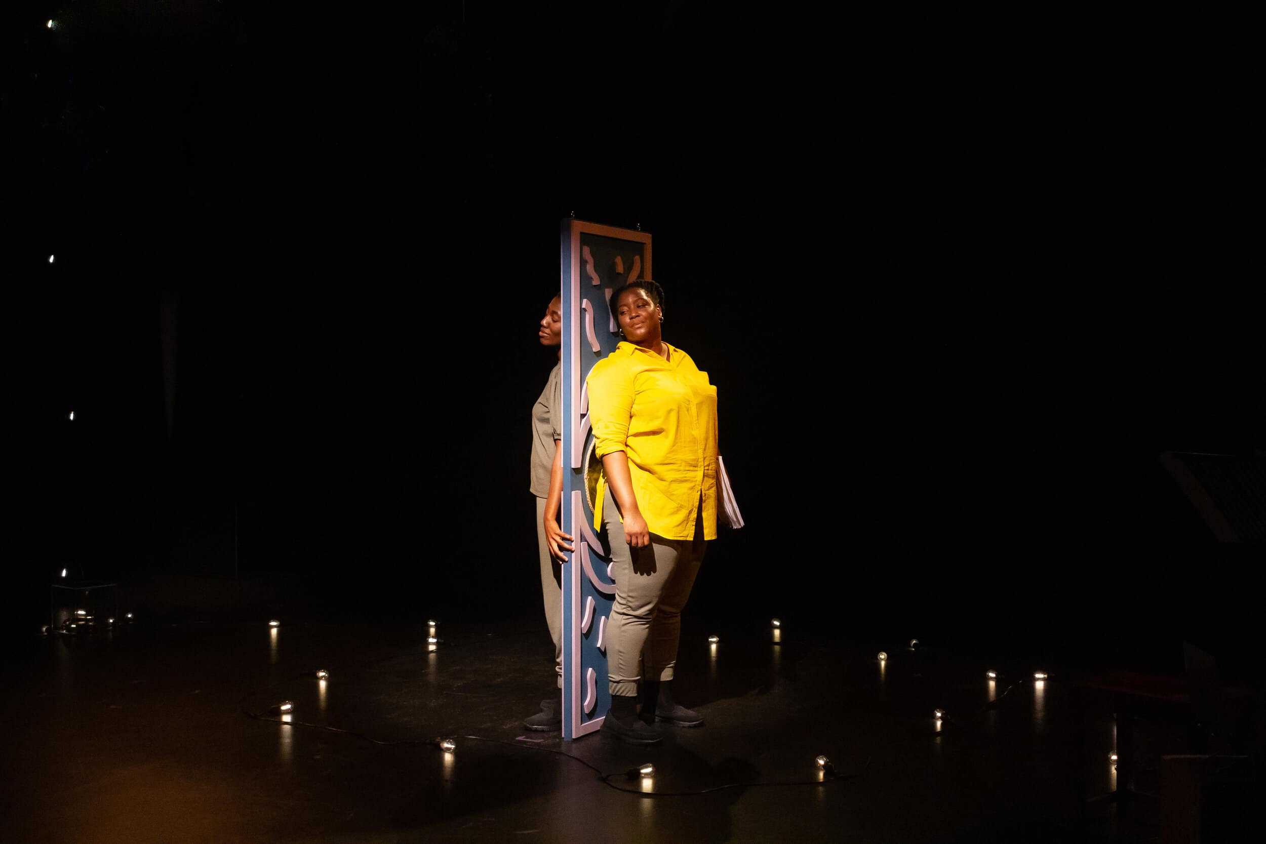 Scene from the Theatre Show Tomorrow Is Not Promised showing two black women standing back to back a rectangular plank