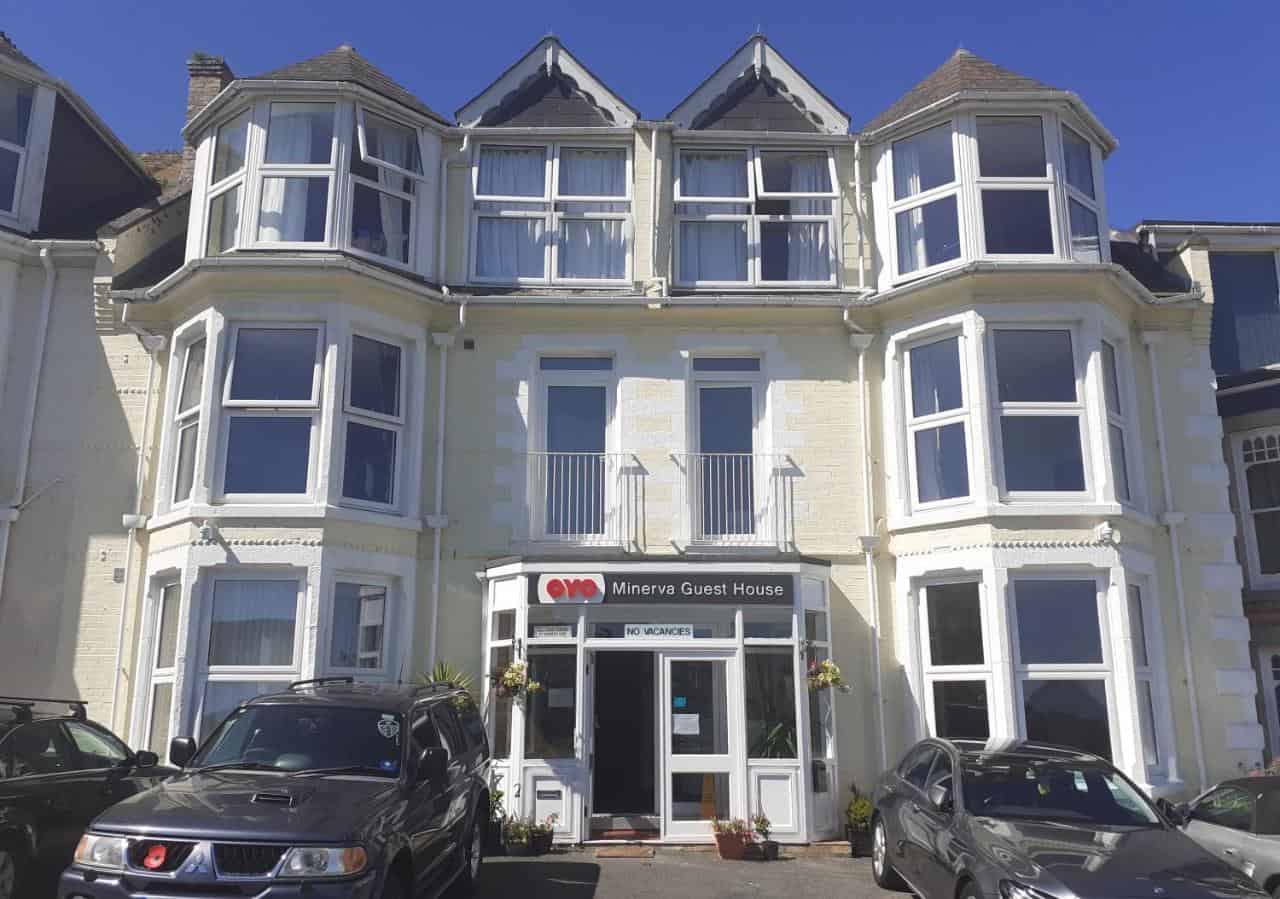 Sunny facade of Minerva Guest House with parked cars.