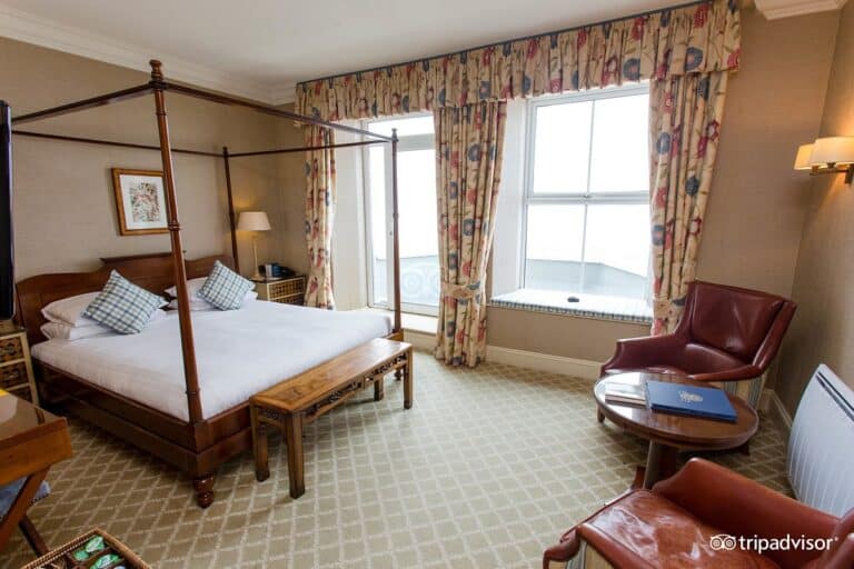 Elegant hotel bedroom with four-poster bed and sea view.