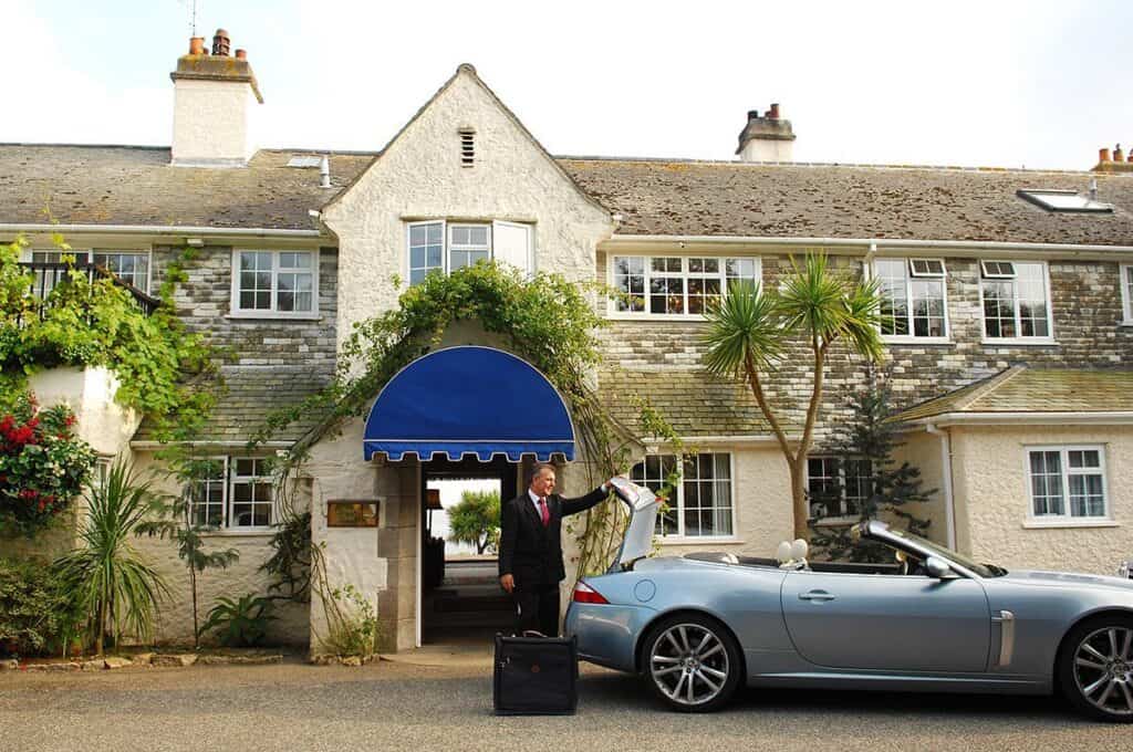 Chauffeur greeting outside luxury hotel with convertible car.