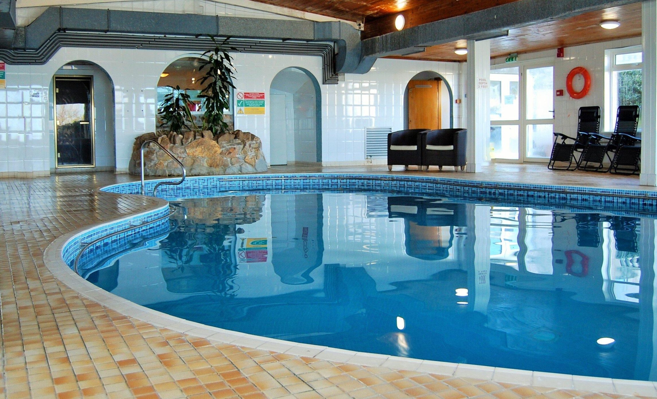 Indoor hotel swimming pool with chairs and plants.